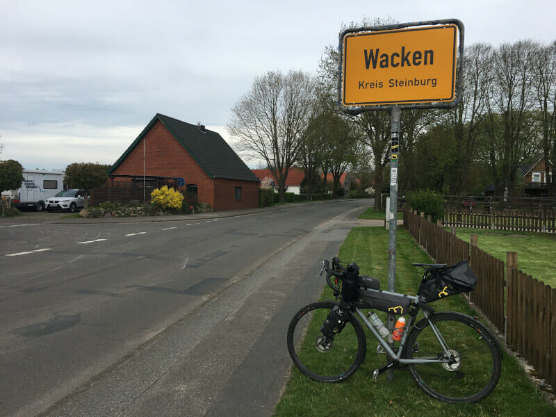 Wacken - Ortsschild mit Gravelbike - Nord-Ostsee-Kanal-Radweg.